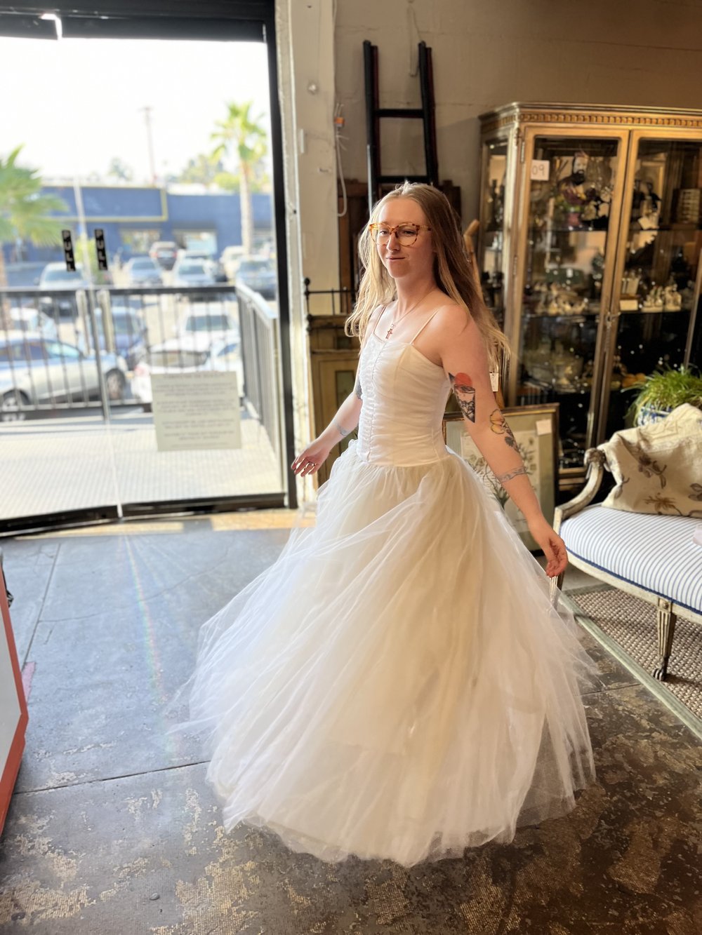 A girl in a vintage antique shop in a white 1990's fiesta wedding dress twirling.