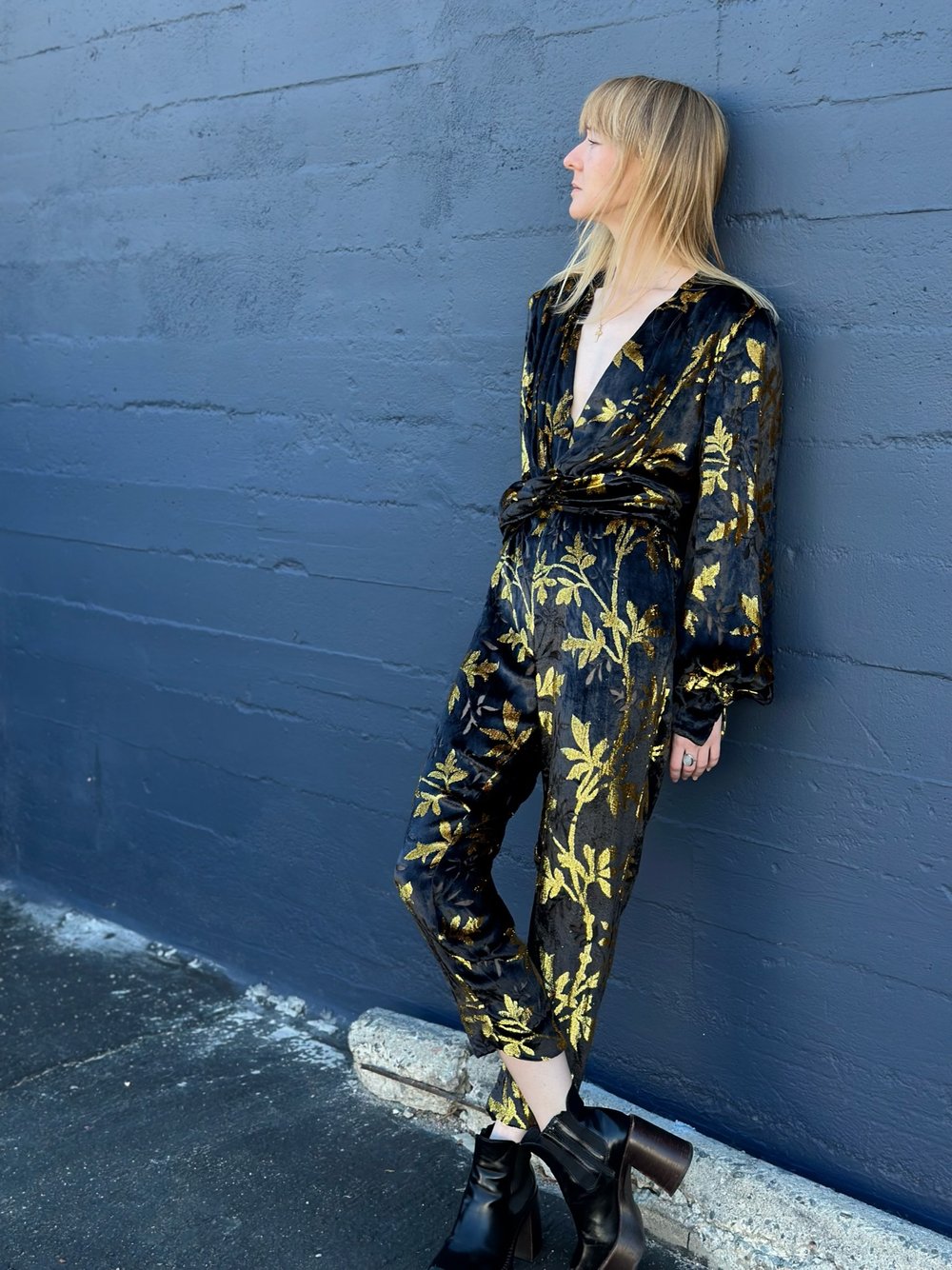 A girl leaning her back against a blue wall outside, wearing a 2010's Anatalya Jumper.