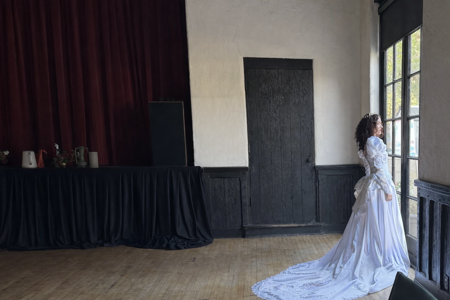 Woman in a white vintage bridal dress standing in a room with a large window.