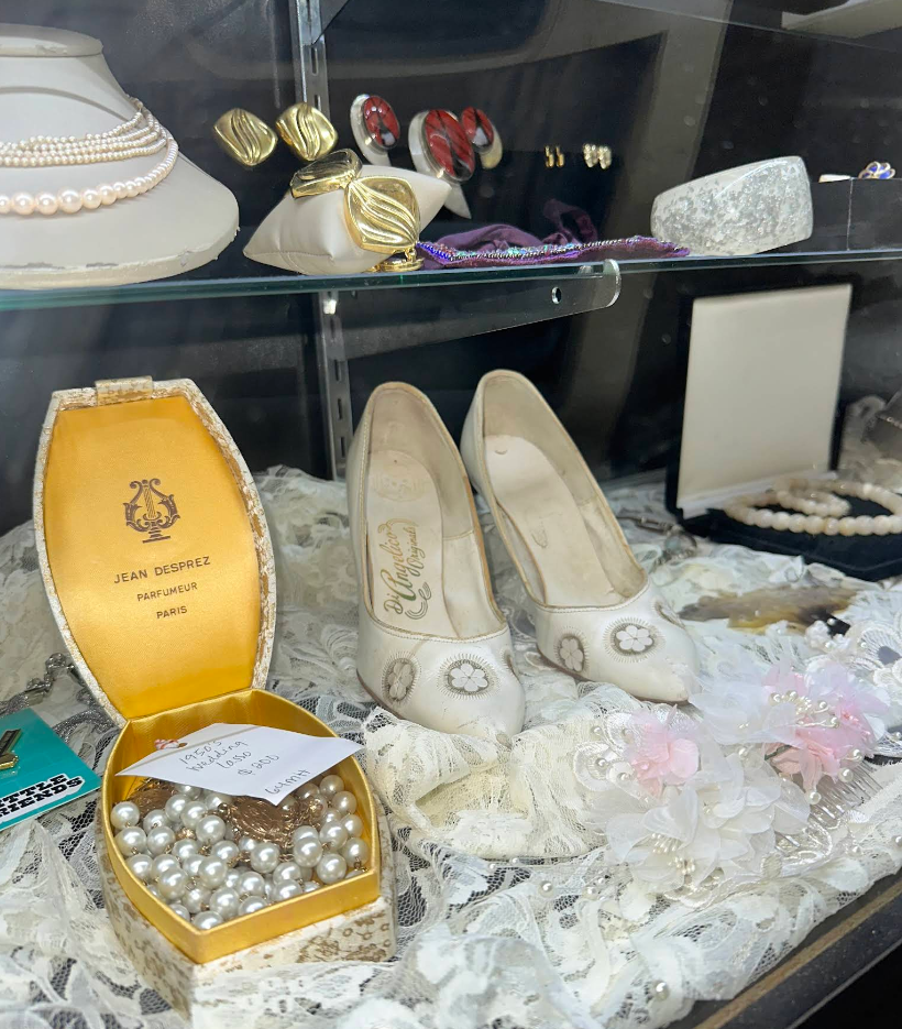 Display of vintage shoes, jewelry, and accessories including a box of pearls and a gold shoe box.