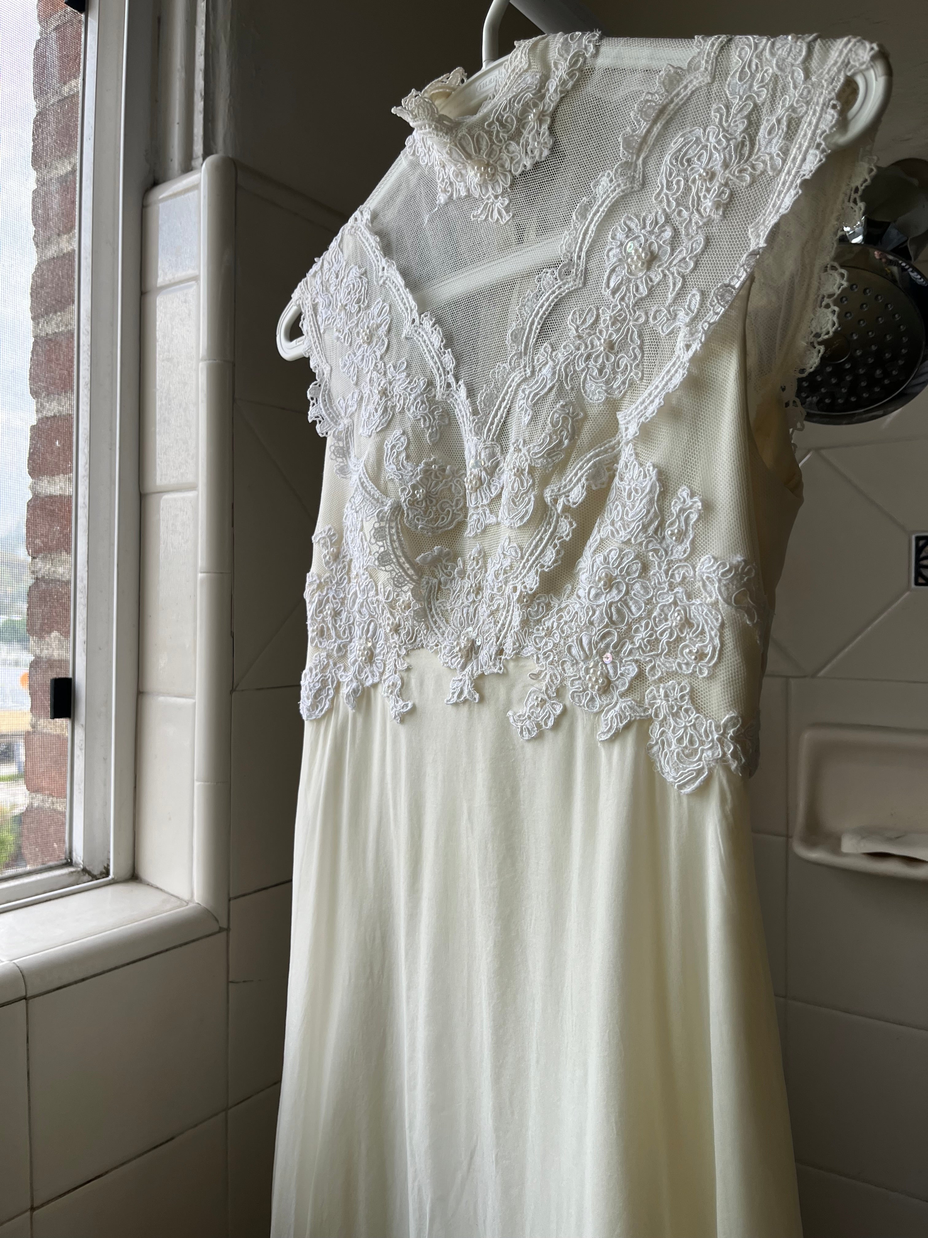 White lace wedding dress hangs by coat hanger in shower on curtain rod